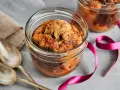 Zwei köstliche Kuchen im Glas, mit Schokoladenstückchen, warten auf Löffel. Eine pinke Schleife und Leinentuch deuten auf ein besonderes Geschenk hin.