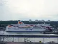 Prom Tallink płynie z Tallinna do Sztokholmu. Statek z kolorowymi pasami na burcie cumuje w porcie.