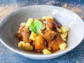 Delicioso cordero al chilindrón en un cuenco gris, acompañado de patatas fritas y una ramita de perejil.