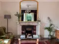 Sofá verde, chimenea con espejo dorado y candelabros. La sala de estar exhibe colores elegantes y un ambiente acogedor.