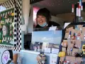 Lachende Verkäuferin auf dem Flohmarkt Friedrichshagen präsentiert handgefertigten Schmuck, darunter Eulen-Ohrringe und Miniatur-Flaschen.
