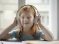 Ruda dziewczynka z zamkniętymi oczami słucha audiobooka przez słuchawki, zanurzona w świecie historii.
