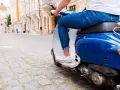 Un uomo in jeans guida uno scooter blu su un lastricato, un'immagine che evoca la libertà e lo spirito dell'art 52 cds.