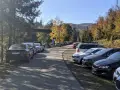 Wielka racza samochodów na leśnym parkingu. Jesienne drzewa i góry w tle.