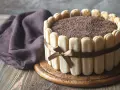 Wykwintny tort tiramisu, otoczony biszkoptami i ozdobiony czekoladową posypką, prezentuje się apetycznie.