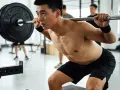 Un homme transpire en faisant un squat avec une barre chargée, un exercice clé pour un programme musculation prise de masse.