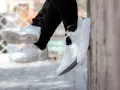 Białe buty, w tym klasyczne Air Force 1, wiszą na nogach w czarnych spodniach.
