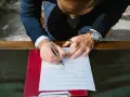 Mężczyzna w garniturze podpisuje dokument. Zastanawia się, jakim nazwiskiem podpisać się na ślubie cywilnym, wybierając to właściwe.