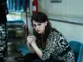 Carmela, con sguardo intenso, attende il suo destino fuori dal carcere. Indossa una camicia leopardata.