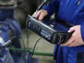 Technik w niebieskim kombinezonie wykonuje pomiary drgań maszyny przemysłowej za pomocą przenośnego urządzenia.