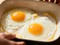 Deux œufs au plat dans un plat en céramique, parfaits pour une recette avec beaucoup d'œufs. Du beurre fond doucement.