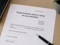 Dokument "Wypowiedzenie umowy o pracę na czas określony" z polem na wpisanie przyczyny. Długopis czeka na podpis.