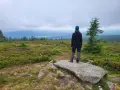 Widok z najwyższego szczytu Gór Izerskich. Kobieta w czapce i kurtce podziwia rozległą panoramę.
