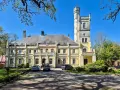 Żółty pałac w Rybokartach z wieżą, otoczony zielenią.