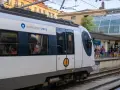 A white Euskotren train waits at the Amara station, ready to take passengers from Hendaye to San Sebastian. People stand on the platform, some boarding.