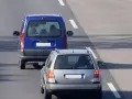 Un veicolo che precede, una monovolume blu, è seguito da un'auto station wagon argentata su una strada asfaltata con segnaletica bianca.