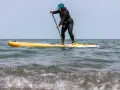 Frau auf einem gelben Stand Up Paddle Board im Meer, mit Paddel in der Hand.