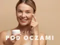 Uśmiechnięta kobieta aplikuje krem pod oczy. To rozwiązanie na cienie pod oczami, które przywróci blask Twojej skórze.