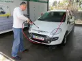Mężczyzna myje białe auto na myjni. Na tablicy informacyjnej widnieje napis "Możliwość otrzymania faktury", sugerujący, że na myjni można płacić kartą.