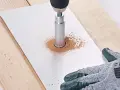 Une perceuse avec une couronne diamantée réalise une découpe carrelage, créant un nuage de poussière fine sur une plaque blanche.