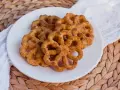 Buñuelos dorados con azúcar y canela en un plato blanco.