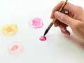 Une main peint des fleurs à l'aquarelle. Un bouquet de fleurs peinture facile, avec des touches de rose, jaune et pêche.