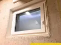 Ein neues, weißes Kellerfenster ist in eine Betonwand eingesetzt. Der Austausch des Kellerfensters verbessert die Dämmung und Sicherheit.