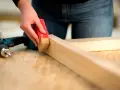 Eine Hand schleift mit einem roten Schleifklotz ein Holzstück. Daneben liegt ein Akkuschrauber.