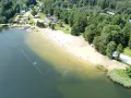 Słoneczny dzień nad jeziorem Rogoźnik. Ludzie kąpią się i opalają na piaszczystej plaży, otoczonej zielonym lasem.