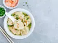 Aksamitna zupa wonton z krewetkami i szczypiorkiem, podana z pałeczkami.