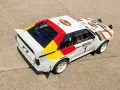 Biały rajdowy **Audi quattro S1** z kolorowymi pasami i logotypami sponsorów, gotowy do podboju szutrowych tras.