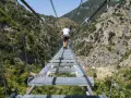 Un ponte tibetano in Puglia attraversa una gola verdeggiante, con persone che camminano su passerelle metalliche sospese tra montagne.