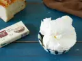 Burro montato soffice in una ciotola, accanto a una confezione di burro salato e una fetta di pane.