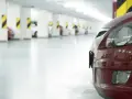 Czerwony samochód na tle rzędu miejsc parkingowych. Zastanawiasz się, ile miejsc parkingowych na mieszkanie jest dostępne?