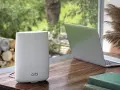 Ein weißer Orbi WLAN-Router steht neben einem Laptop auf einem Holztisch.