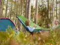 Två tjejer njuter av en lugn stund i en hängmatta på en av Sveriges fina campingar. Bredvid dem står ett tält.