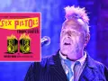 Le chanteur des Sex Pistols, Johnny Rotten, sur scène, avec la pochette de l'album "Never Mind the Bollocks" superposée.