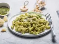 Pyszny makaron z pesto ze słoika i śmietaną, posypany parmezanem. Obok miseczka z pesto i kawałki sera.