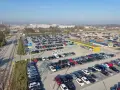Duży parking przy krakow katowice airport. Wiele samochodów zaparkowanych w rzędach, w tle budynki lotniska.