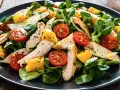 Pyszna sałatka z kurczaka z pomidorkami koktajlowymi i kawałkami mango, podana na ciemnym talerzu.