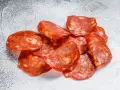Plasterki pikantnego chorizo, wędzonej kiełbasy wieprzowej, z widocznymi kawałkami tłuszczu.