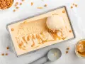 Ein Blech mit cremigem, hellbraunem Salted Caramel Eis, garniert mit Karamellsauce und kleinen Karamellwürfeln. Eine Eiskugel liegt darauf.