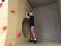 Ein fröhliches Mädchen klettert in einer Kletterhalle für Kinder. Sie lächelt und hält sich an einem Griff fest.