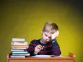 Zmęczony chłopiec z podpartą głową przy biurku, gdy szkoła nie realizuje zaleceń poradni. Stos książek obok.