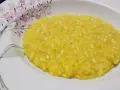 Un cremoso risotto allo zafferano, servito in un piatto bianco decorato con fiori rosa e rami verdi.
