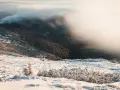Zimowy krajobraz górski, gdzie mgła otula lasy, a śnieg pokrywa zbocza. Widok przypomina kocioł wielkiego stawu, otoczony mroźnym pięknem.