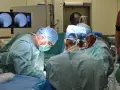 Chirurdzy w maseczkach i czepkach operacyjnych pochyleni nad pacjentem.