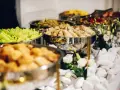 Bufet z jedzeniem: naleśniki, sałatka, smażone potrawy, dekoracje z kwiatów i białych kamieni.