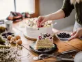 Manos expertas decoran un pastel en una mesa de reposteria y pasteleria, con frutas frescas y arándanos.