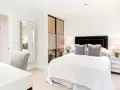Elegante camera da letto senza finestra, con letto bianco, specchio a figura intera e un angolo toeletta.